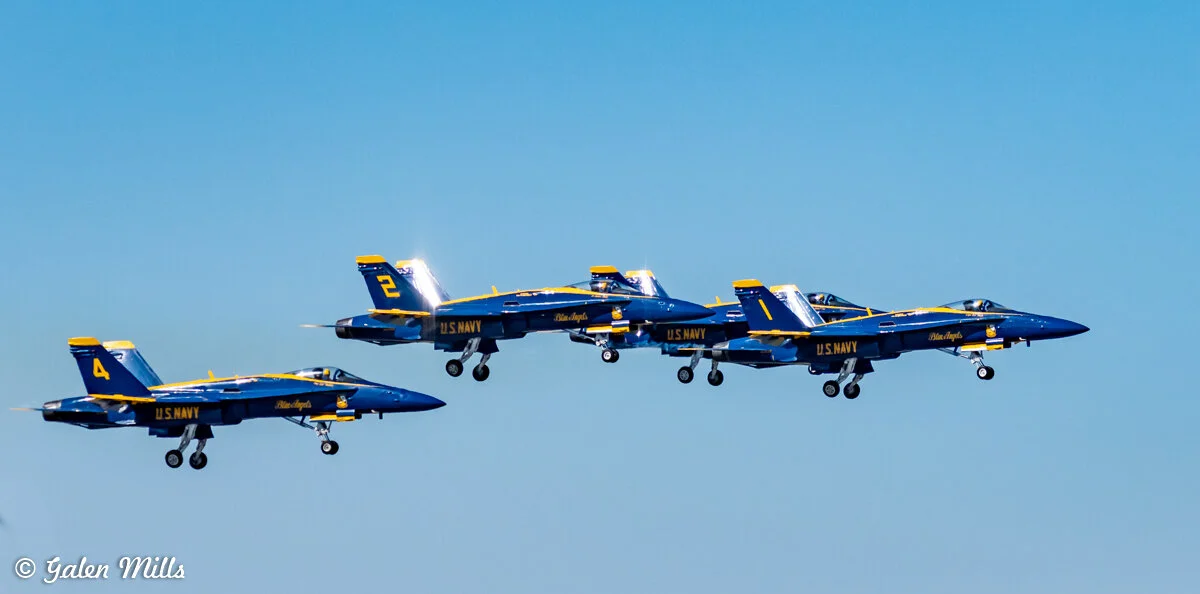 Four Blue Angels jets flying in formation against a clear blue sky.