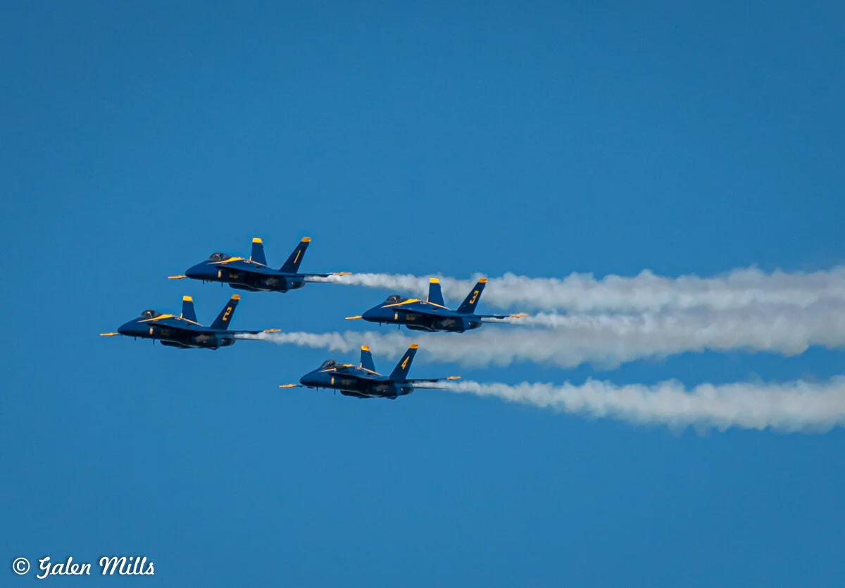 Four military jets flying in formation leaving smoke trails against a clear blue sky.