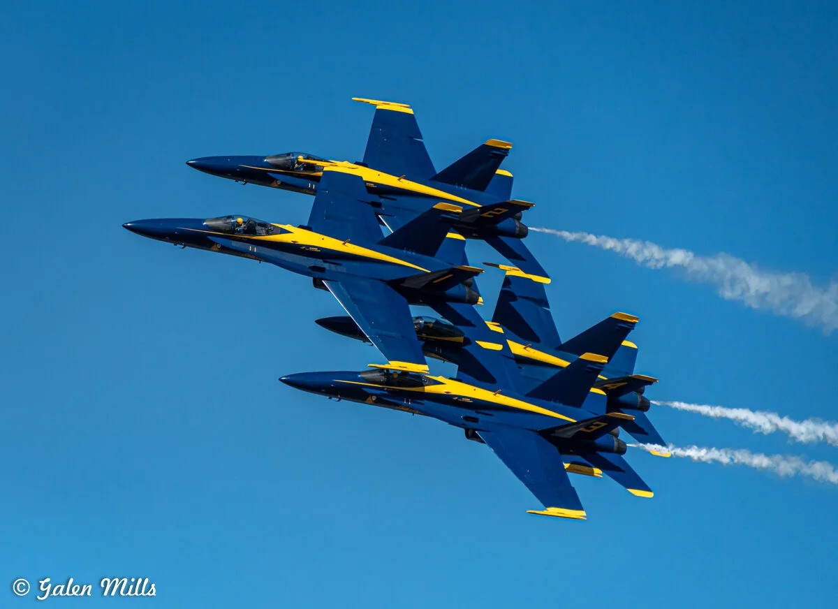 Four Blue Angels jets flying in formation against a clear blue sky.