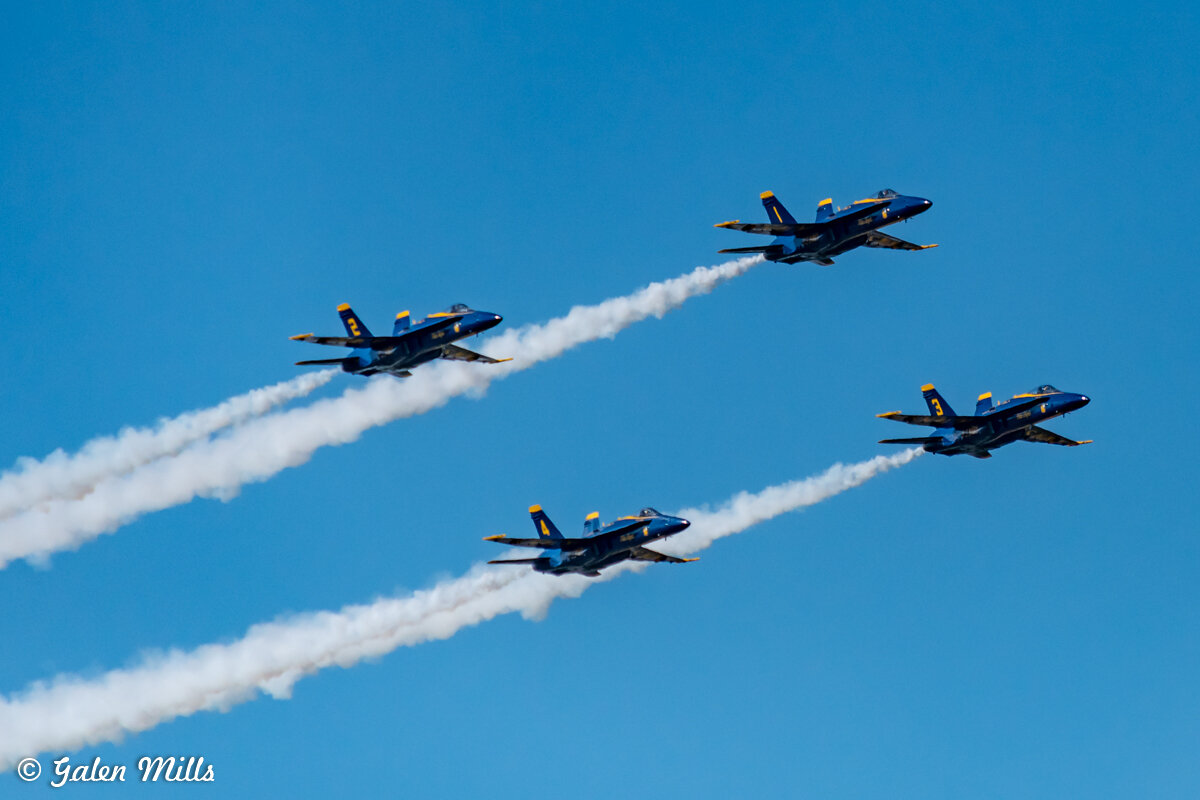 Four jet planes flying in formation with smoke trails against a clear blue sky.