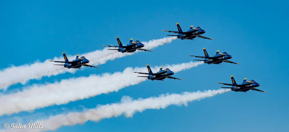 Six fighter jets in formation with trails against a clear blue sky.