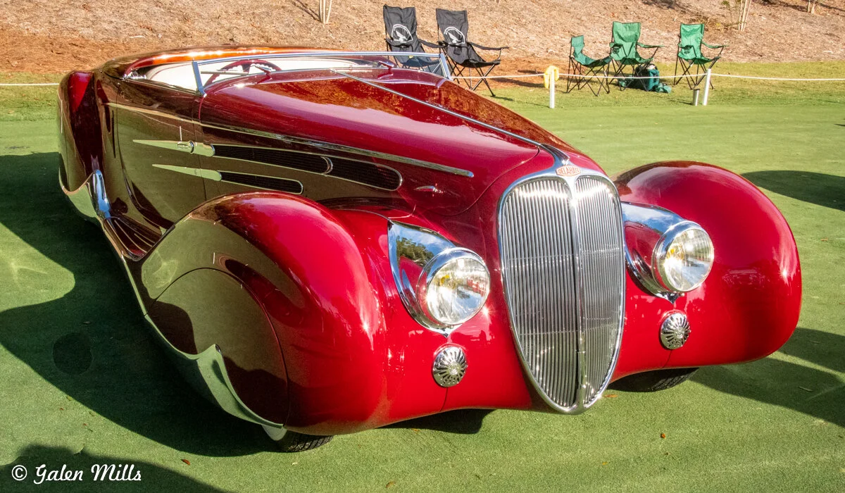 Vintage red car with classic design and chrome accents displayed outdoors on grass.