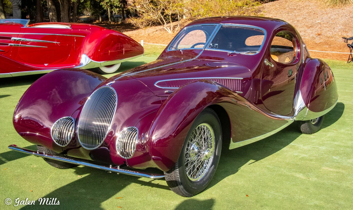 Vintage maroon classic car with sleek, streamlined design and chrome details on a grassy area.