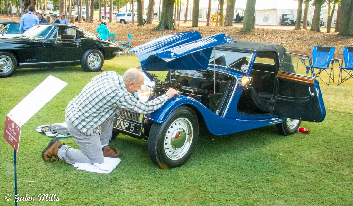 Person inspecting a vintage blue car with hood open at a car show.