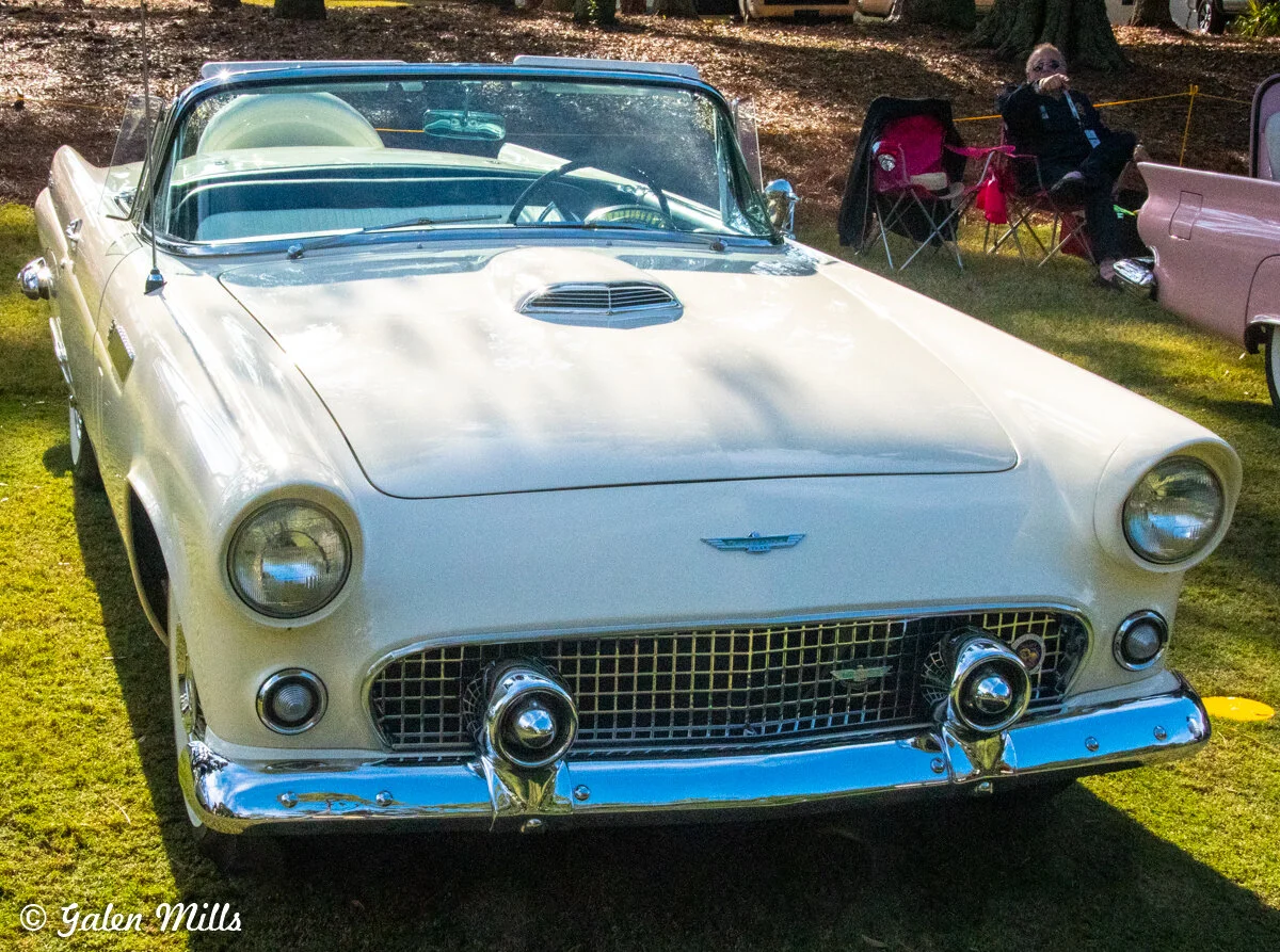 Classic white convertible car with chrome details parked on grass at a car show.