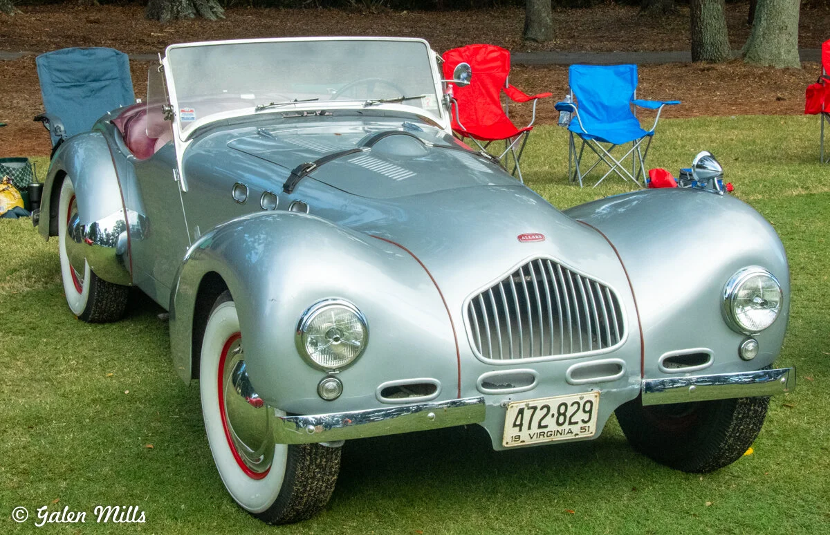 Classic silver convertible car with Virginia license plate parked on grass, surrounded by foldable lawn chairs.