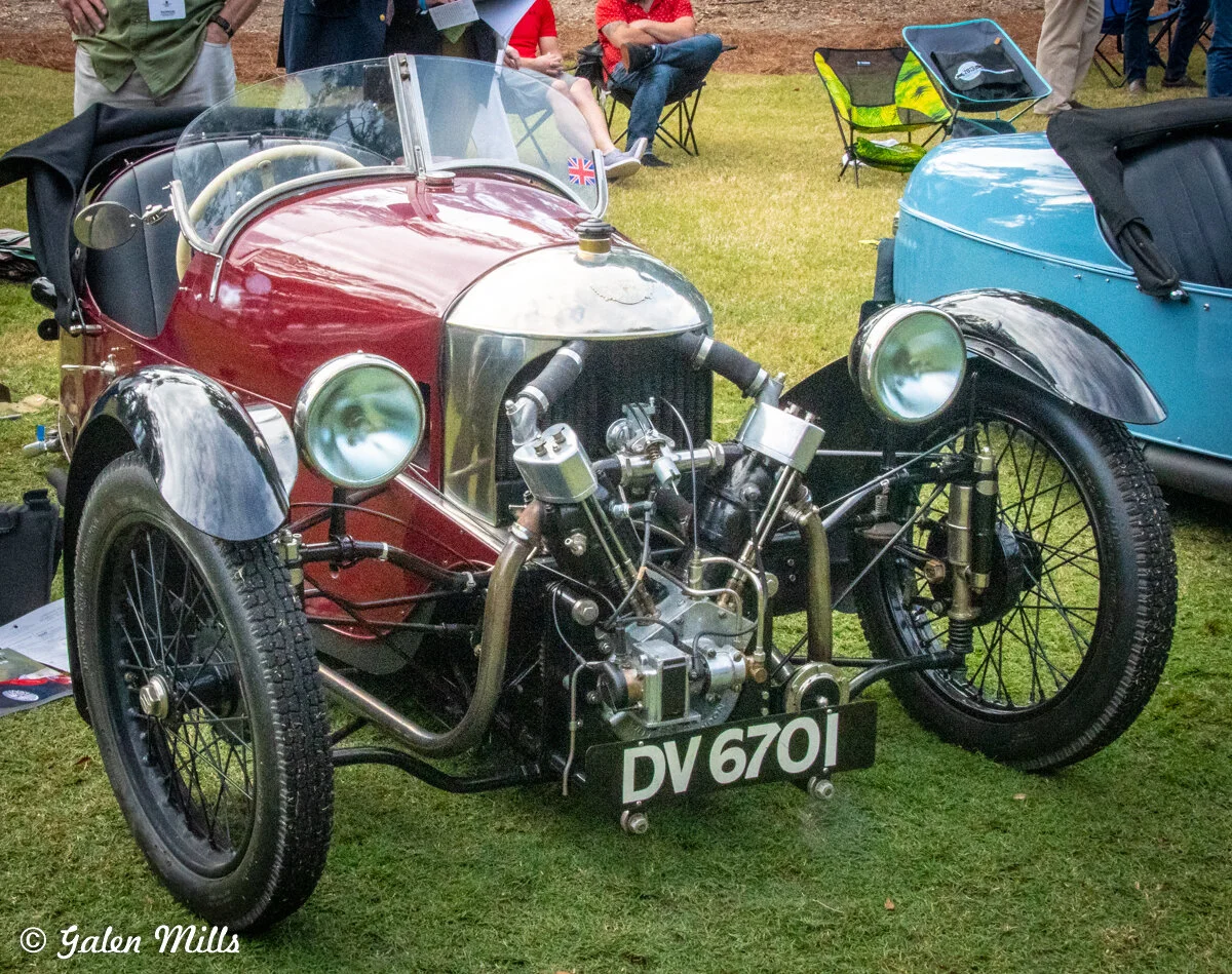 Vintage three-wheeler car with exposed engine and UK flag emblem