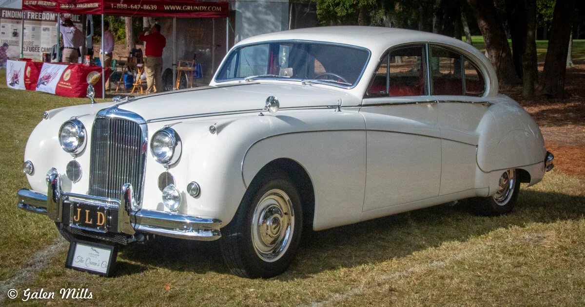 Classic white luxury car on display outdoors with a custom license plate.
