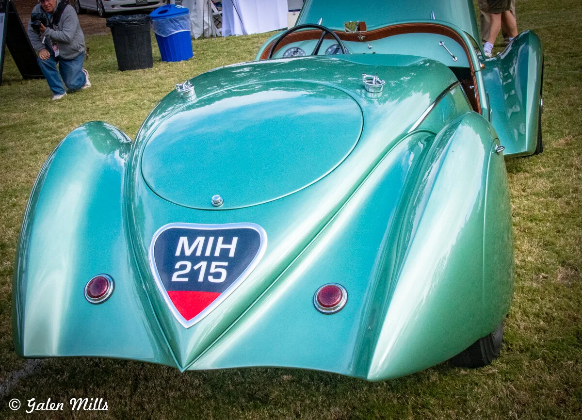 Vintage green car with "MIH 215" license plate at a car show, featuring classic curves and distinct design elements.