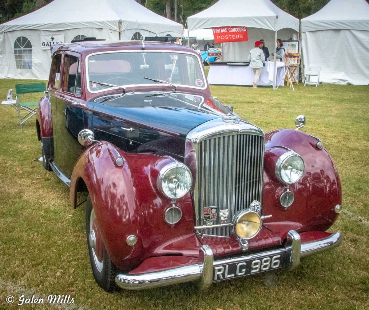 Classic vintage car with maroon and black paint parked on grass, surrounded by white tents. License plate RLG 986 visible.