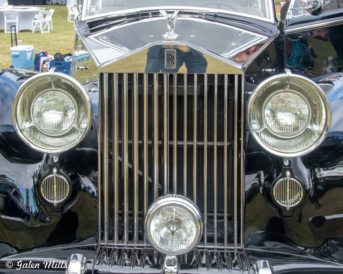 Front view of a classic Rolls-Royce car with a chrome grille and round headlights.