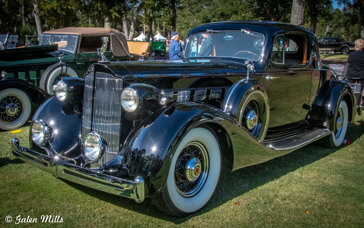 Black vintage car with whitewall tires on grass at a classic car show.