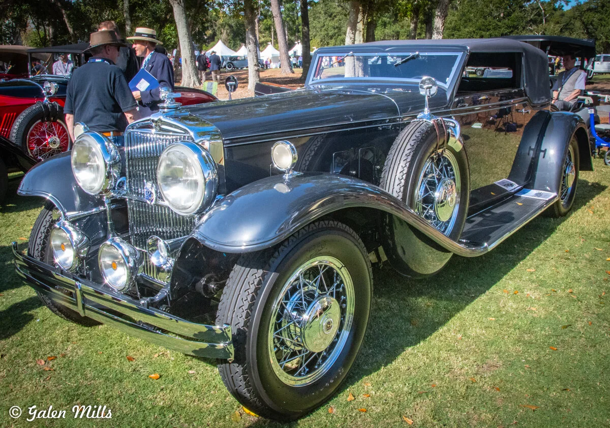 A vintage classic car with chrome detailing, parked on a grassy area at a car show.