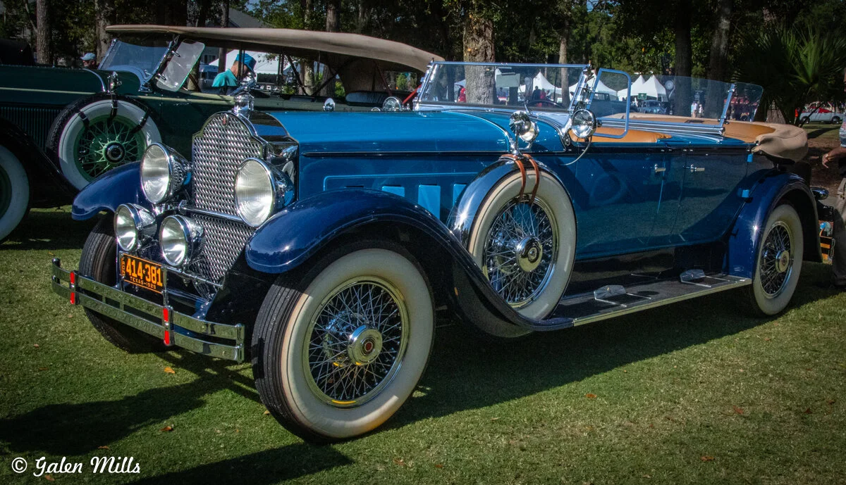 Vintage blue convertible car on display at a car show with whitewall tires and chrome detailing.