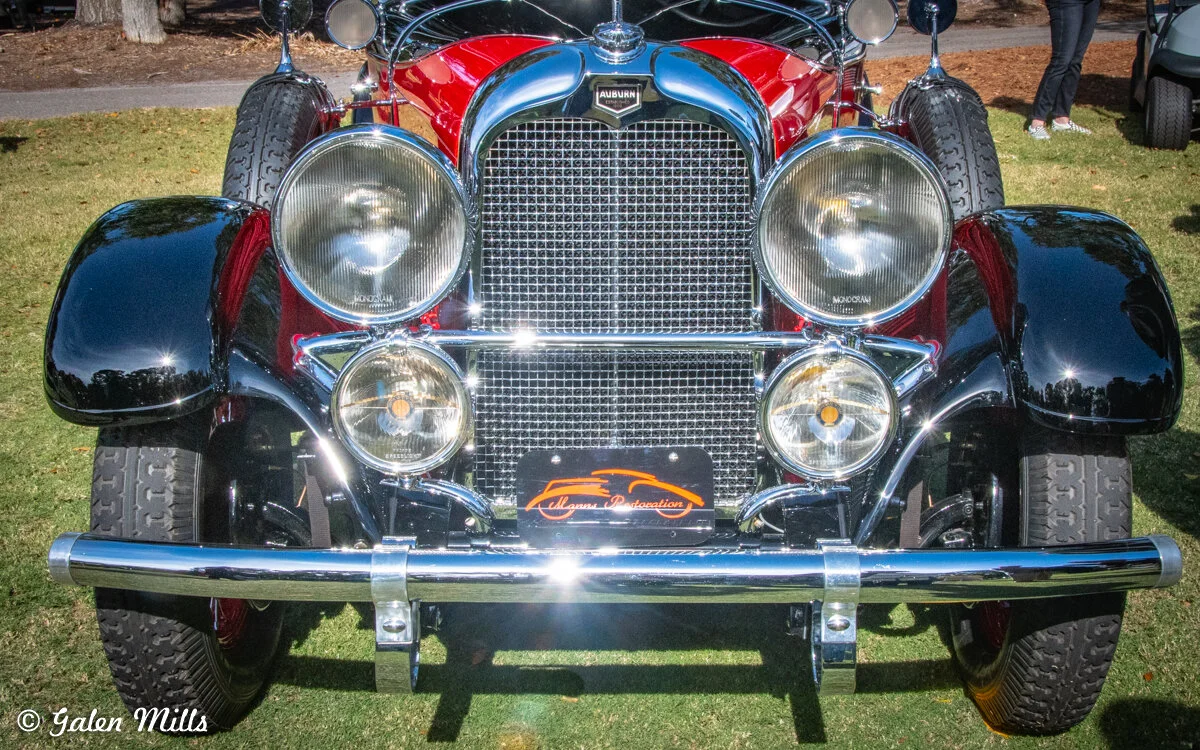 Front view of a classic Auburn automobile with shiny chrome details and round headlights, displayed on grass.