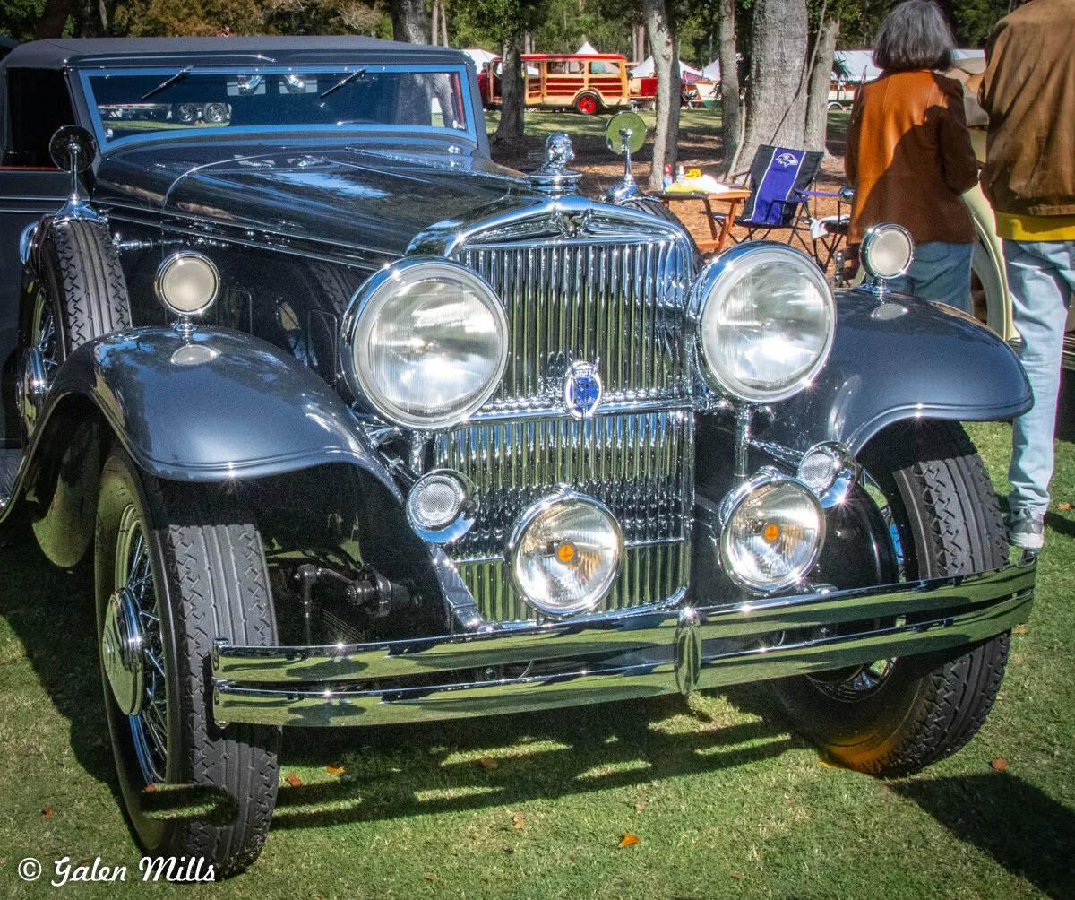 Classic vintage car at outdoor car show with trees and people in the background.