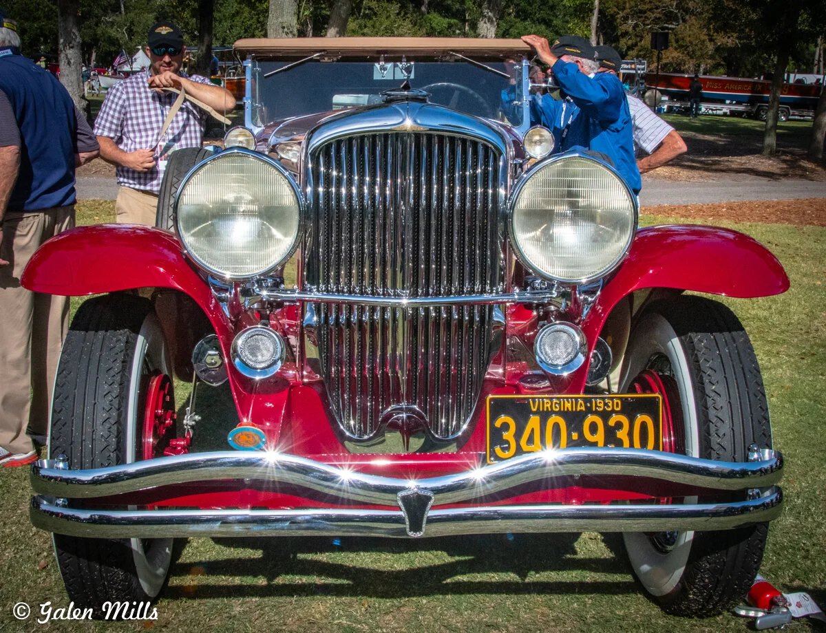 Front view of a vintage red car with a Virginia 1930 license plate at a car show, featuring chrome detailing and large headlights.