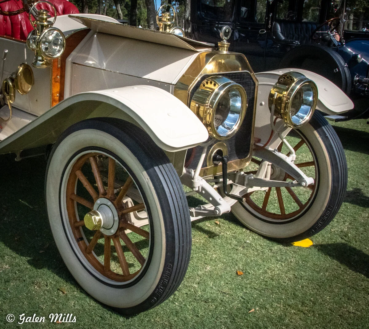 Close-up of a vintage car front with brass headlights and wooden spoked wheels.