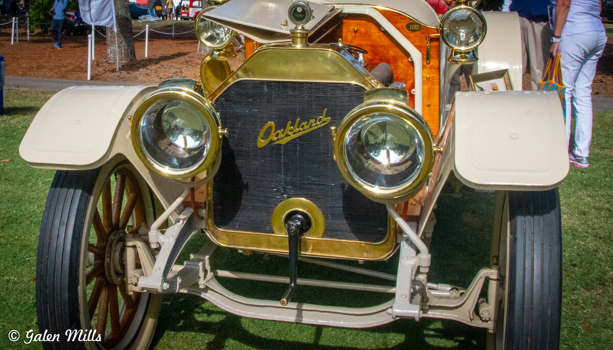 Vintage Oakland automobile with brass fixtures and wooden elements on display at a car show.