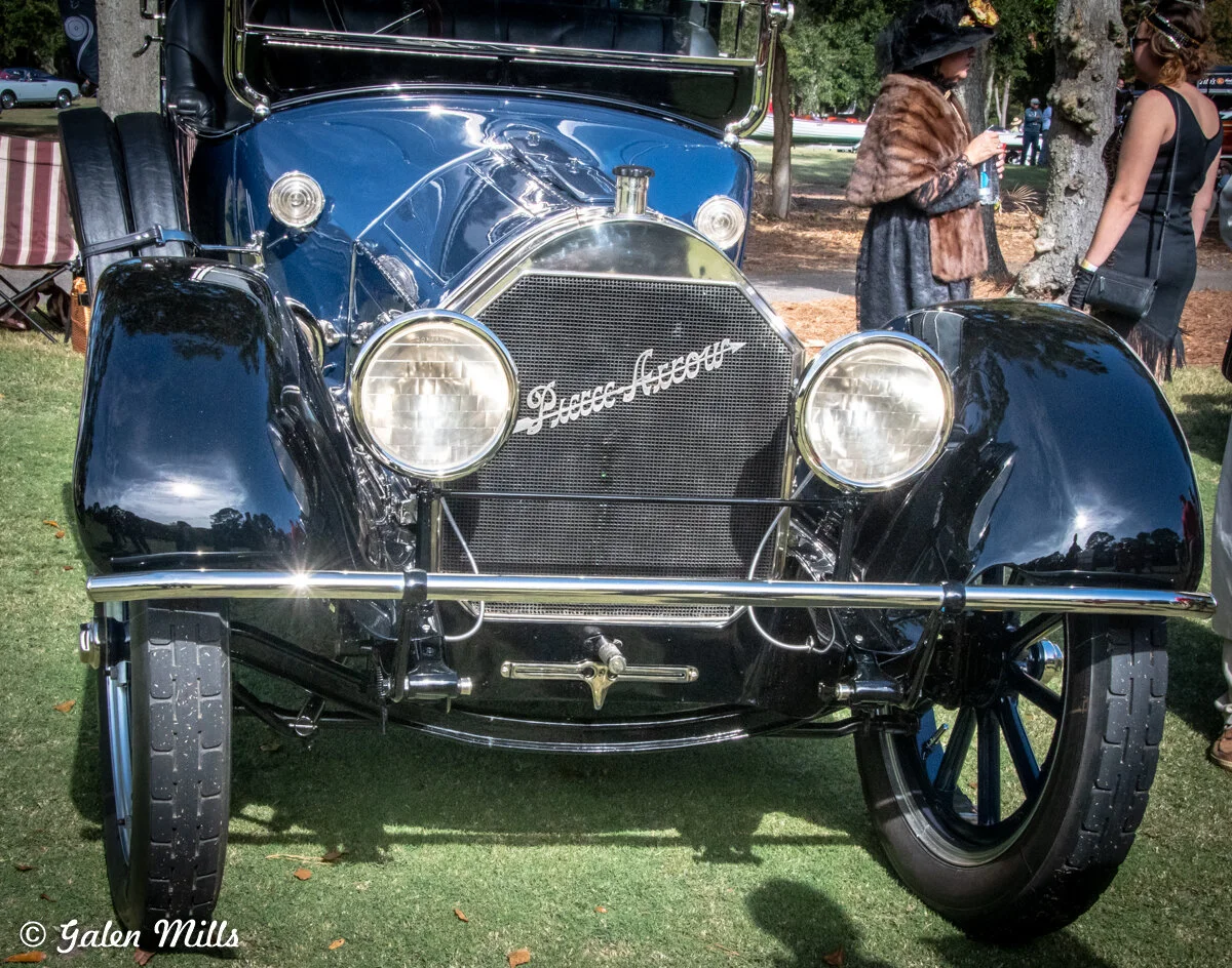 Front view of a classic black Pierce-Arrow car with round headlights, displayed on grass at an outdoor event.