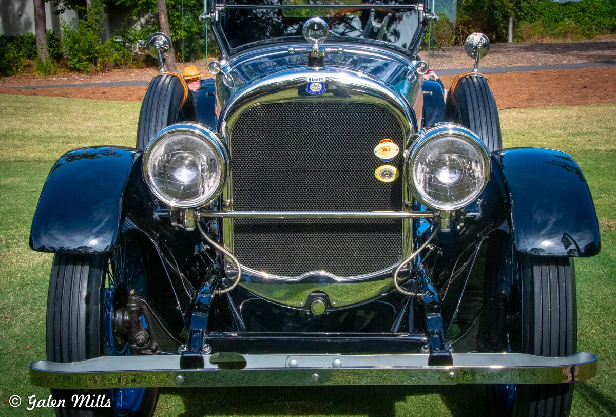 Front view of a vintage Haynes car with round headlights and a chrome grille, displayed on grass.