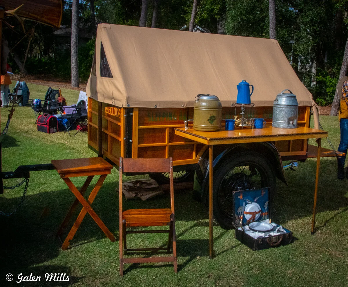 Vintage camping trailer with a canvas cover, wooden furniture, and blue coffee pot on a table in an outdoor setting.