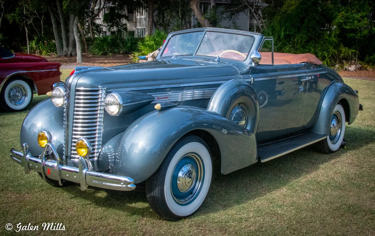 Classic vintage convertible car displayed on grass in a park setting.