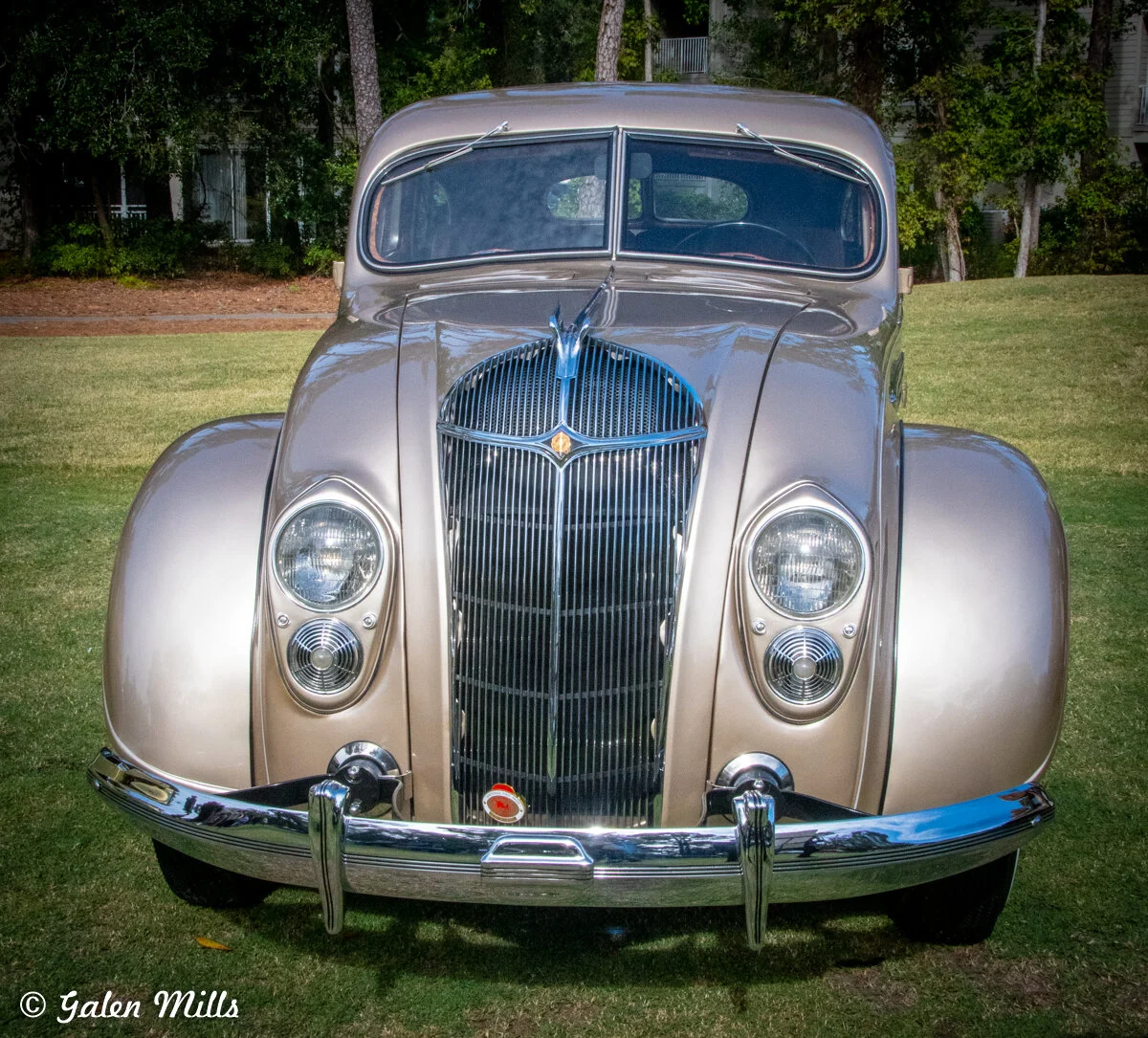 A vintage car with a classic design and rounded headlights, displayed outdoors on a grassy area.