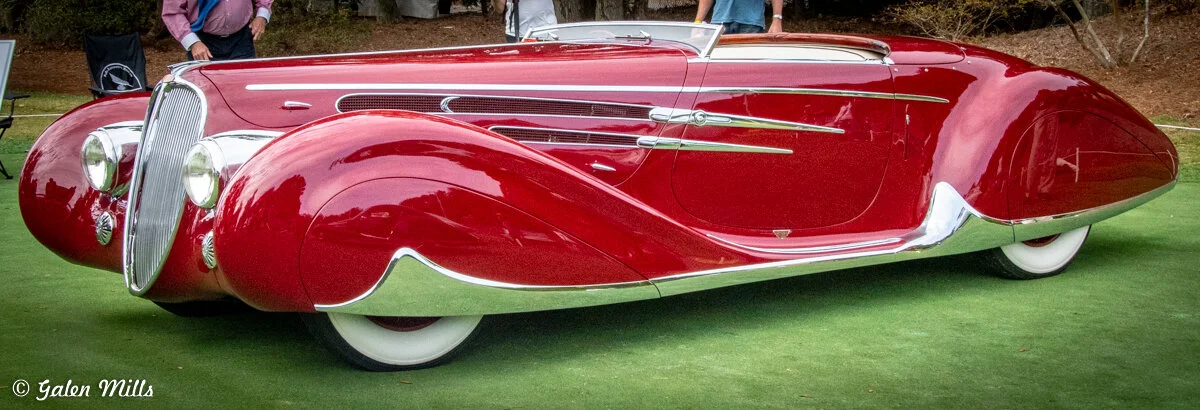 A vintage classic car with glossy red body and chrome accents on display outdoors.