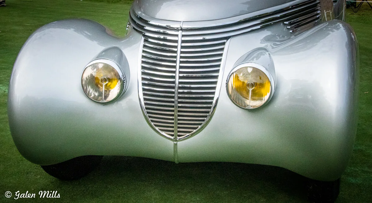 Front view of a vintage silver car with a prominent grille and round headlights.