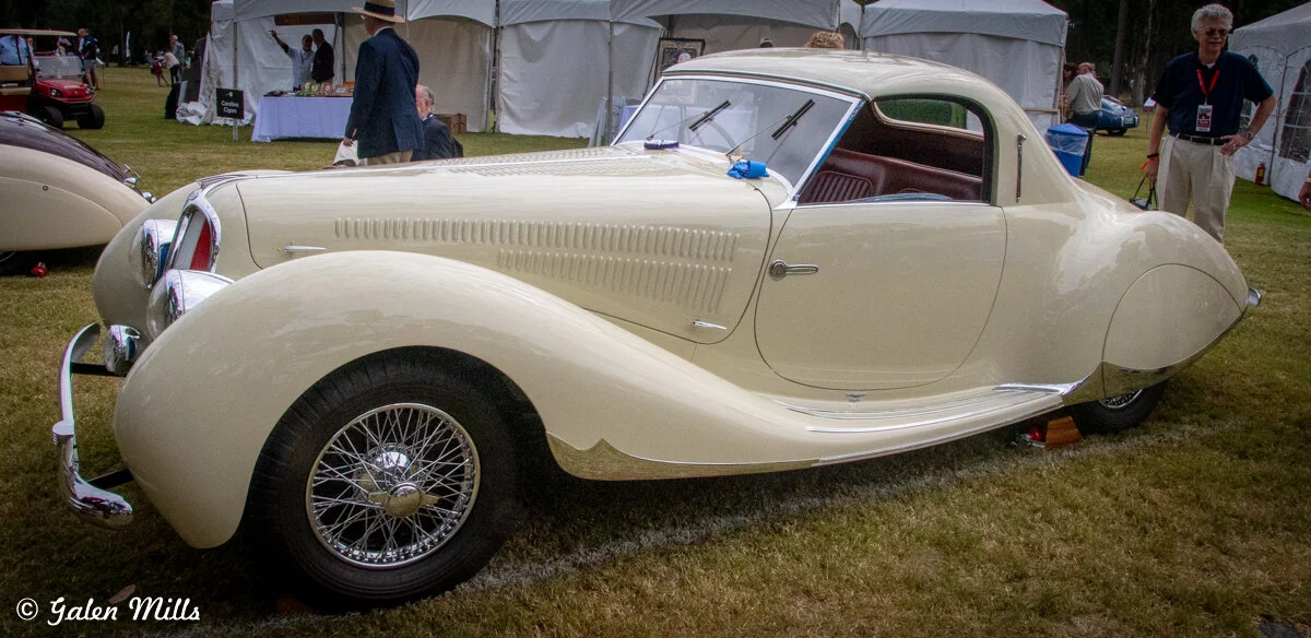 Classic cream-colored vintage car with wire wheels displayed at an outdoor car show.