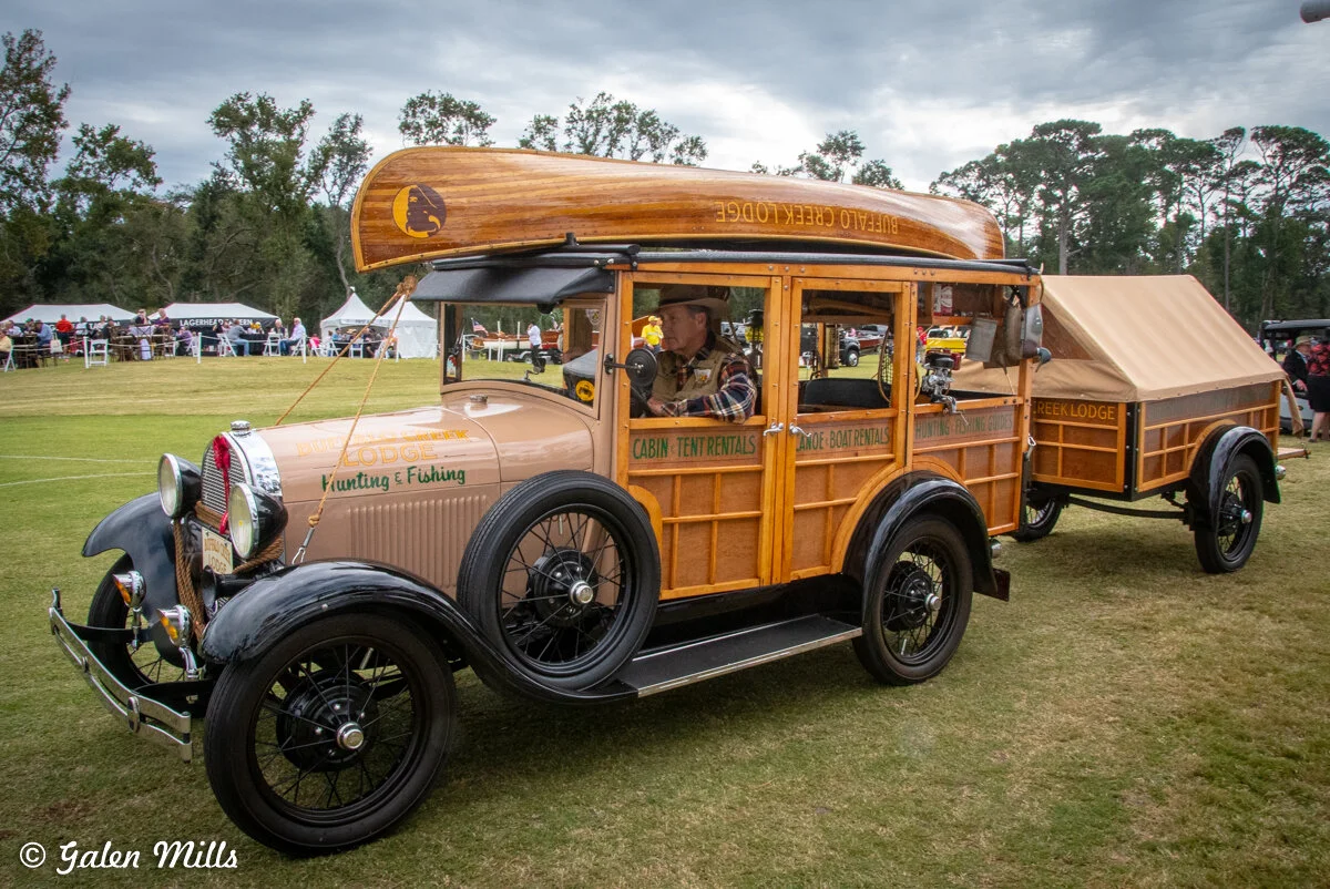 Vintage car with wooden paneling, canoe on top, and matching trailer at an outdoor event.
