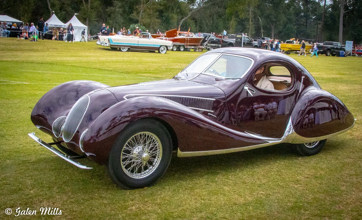 Vintage car at an outdoor car show with people in the background