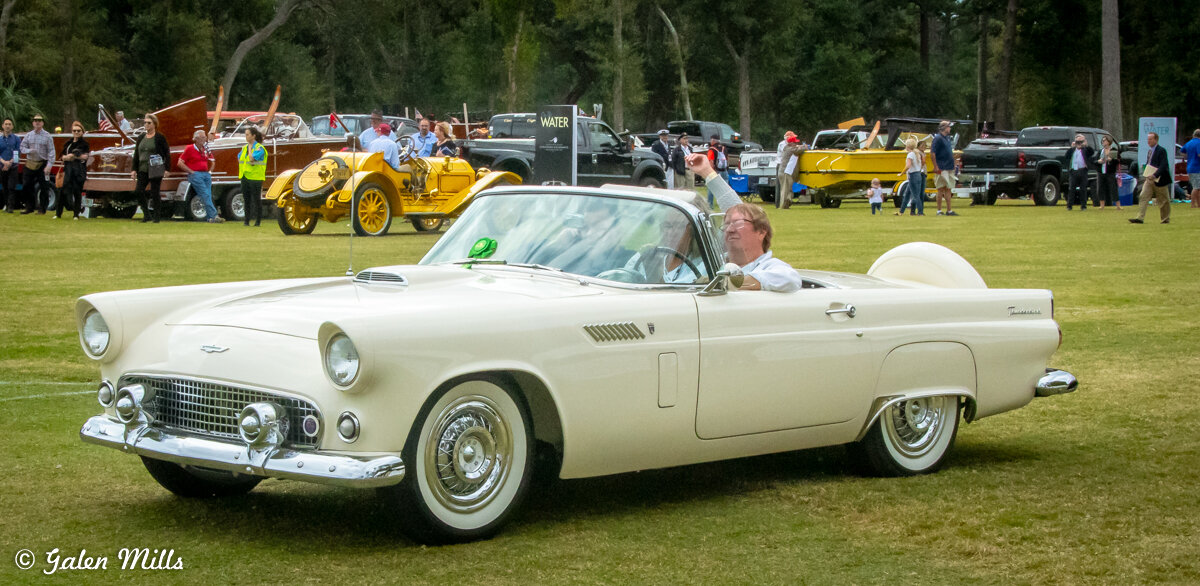 Classic white convertible car at a car show with people in the background.