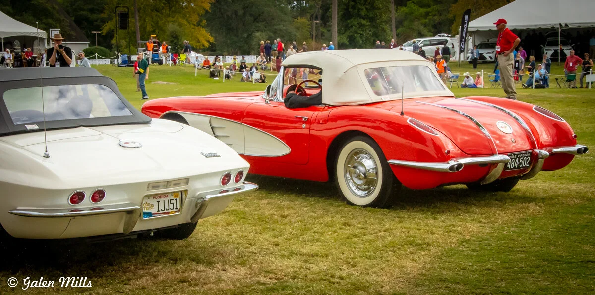 Two vintage Chevrolet Corvettes parked on grass at a car show, with spectators in the background and a white tent nearby.