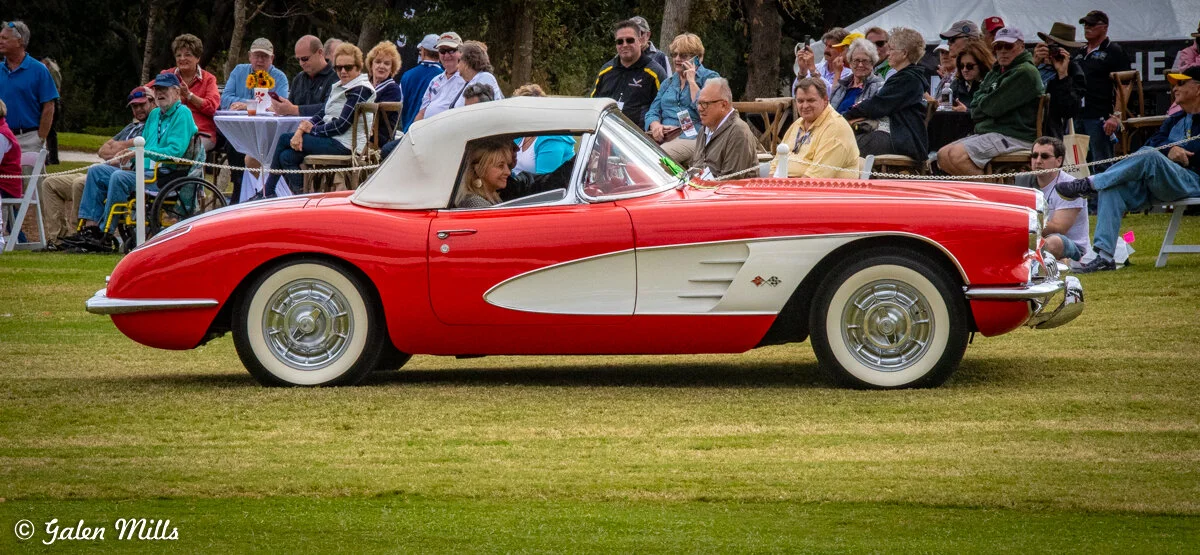 Vintage red convertible car with white accents at a classic car show, surrounded by spectators.