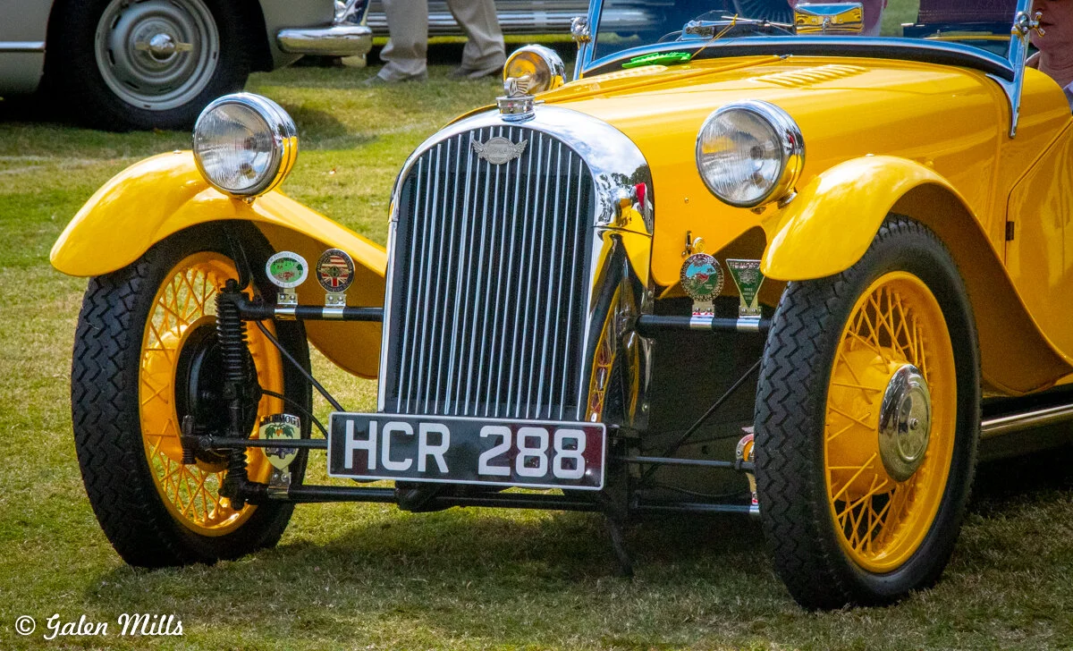 Vintage yellow sports car with a front grille and round headlights, displayed on grass with a license plate "HCR 288."