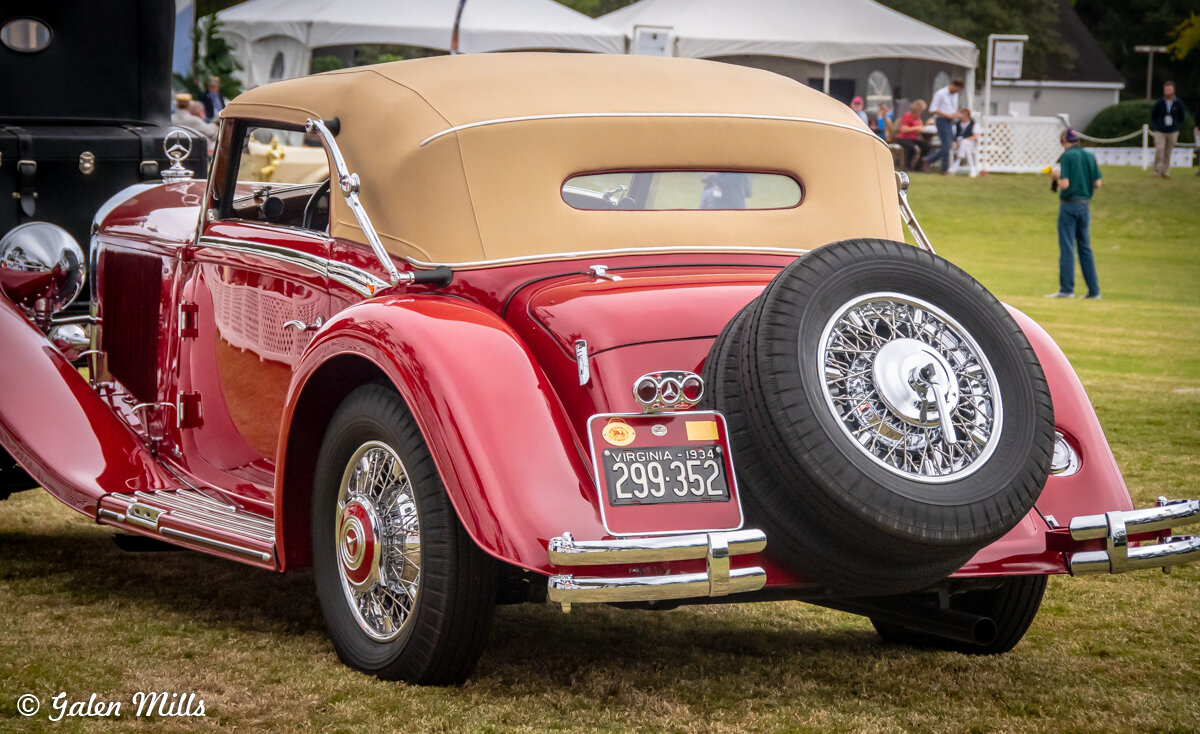 Vintage red convertible car with tan roof and spare tire, displaying a 1934 Virginia license plate, parked on grass at an event.