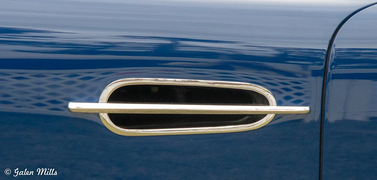 Close-up of a shiny car door handle on a blue vehicle.