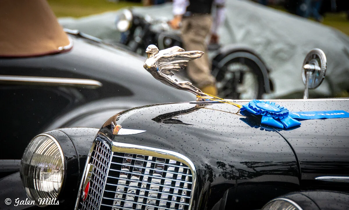 Classic car with hood ornament, rain droplets, and blue ribbon award.