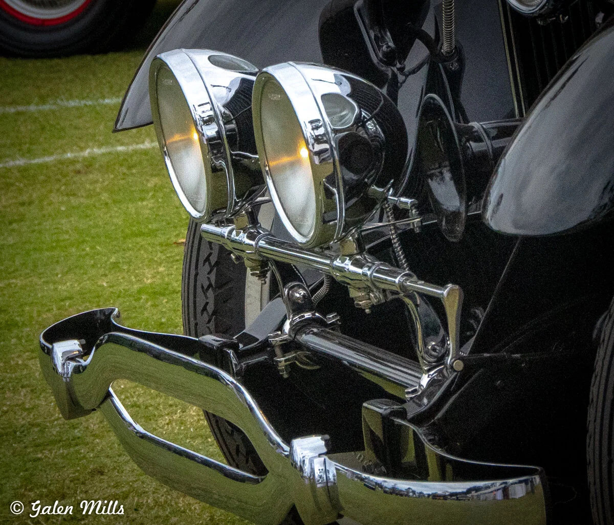 Close-up of the front of a vintage car showing headlights and a chrome bumper.