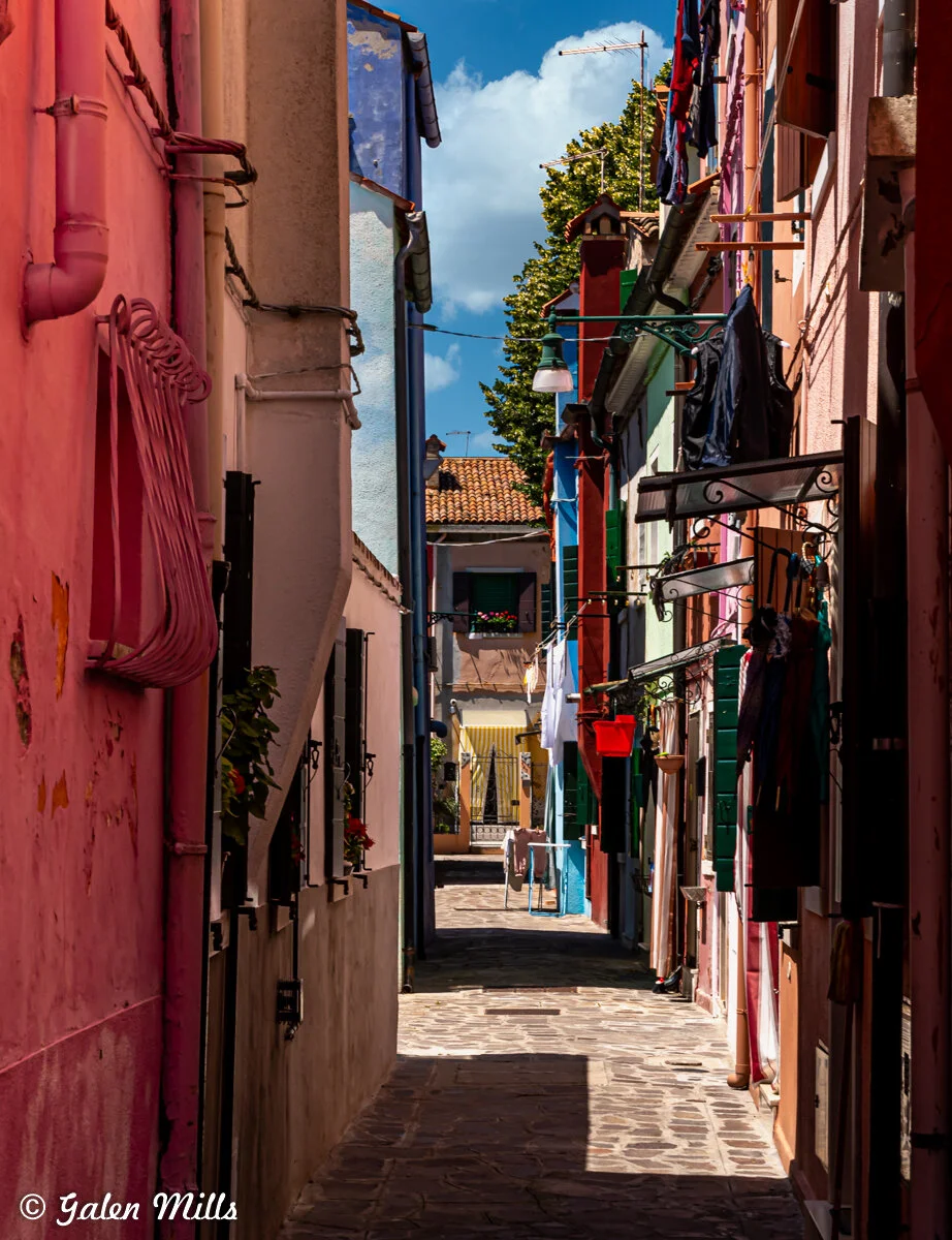 Narrow alley with colorful buildings, cobblestone path, and hanging laundry.