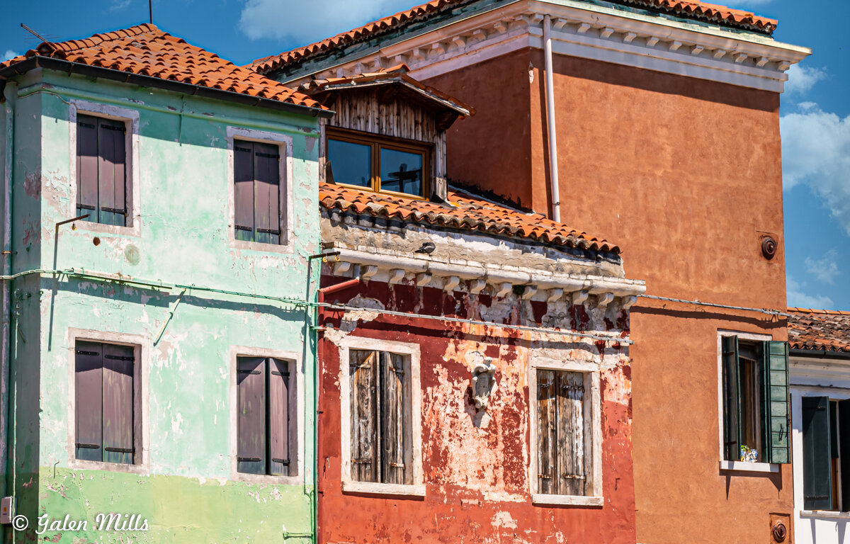 Colorful old buildings with peeling paint and shuttered windows under a blue sky.