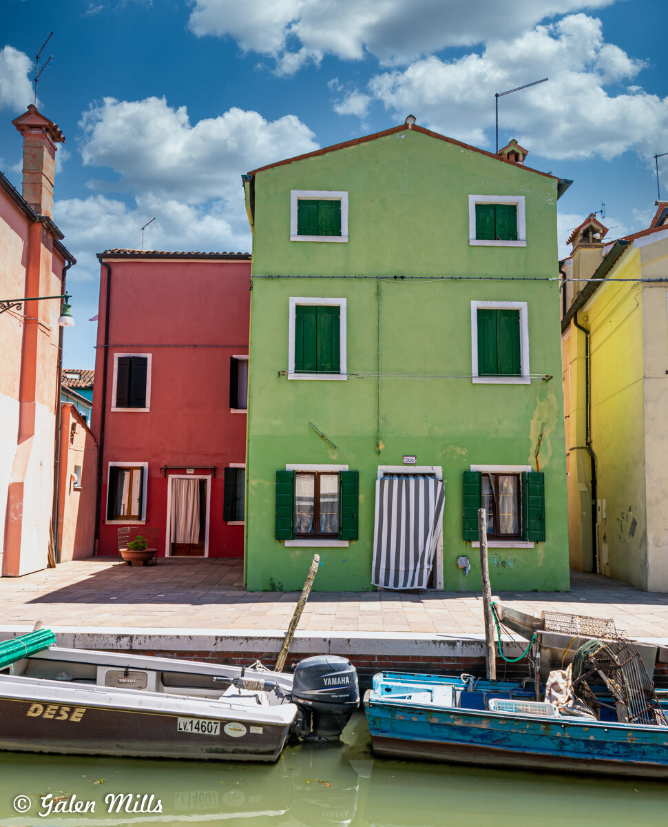 Colorful buildings by a canal with small boats in Burano, Italy.