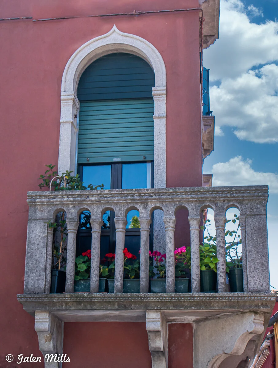 Stone balcony with potted plants and flowers on a historic building in Venice, Italy