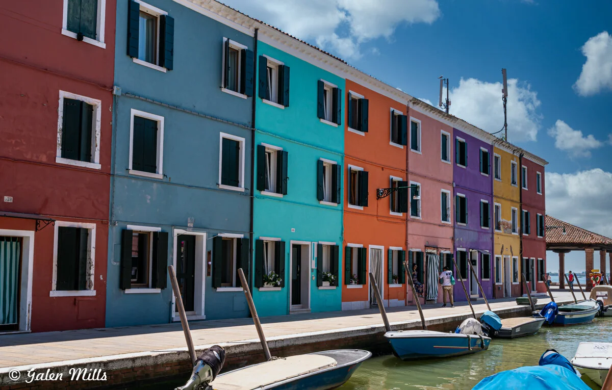 Colorful buildings along a canal with boats in Burano, Italy.