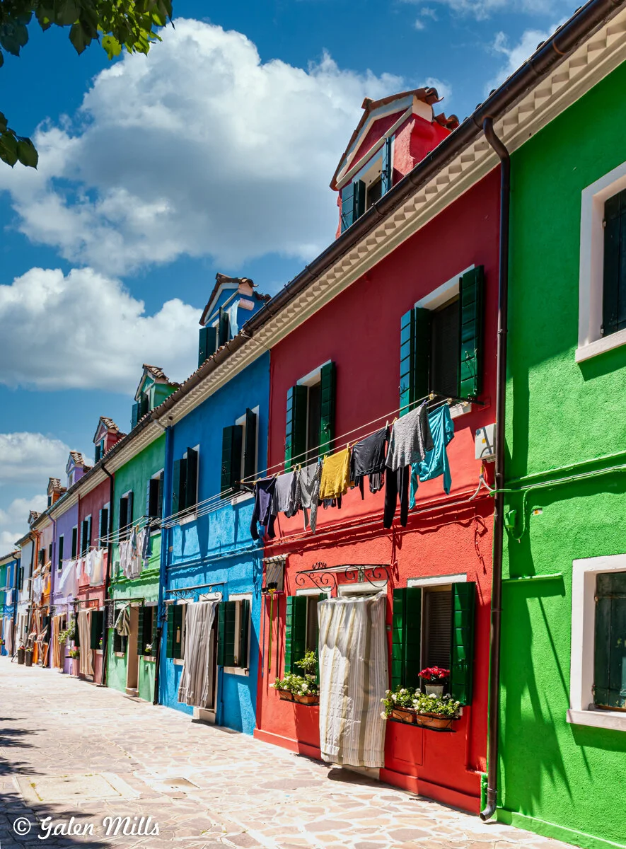 Colorful houses on Burano Island, Italy with laundry hanging, under a blue sky with clouds.