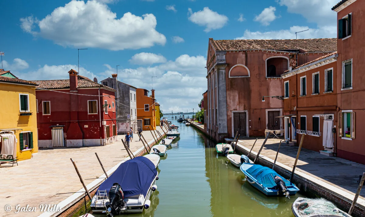 Venetian canal with colorful buildings and boats under blue sky.
