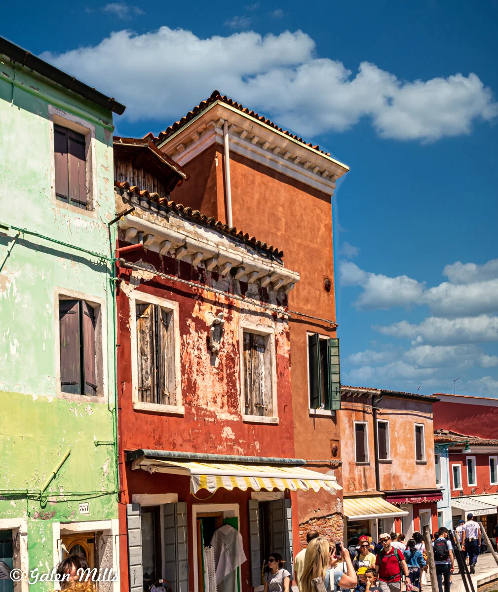 Colorful buildings in Burano, Italy, with peeling paint and people on the street.
