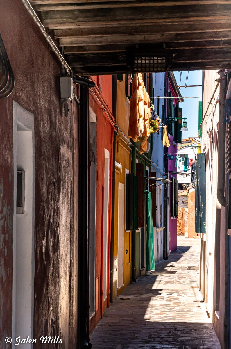 Narrow alley with colorful houses and hanging clothes in Burano, Italy.